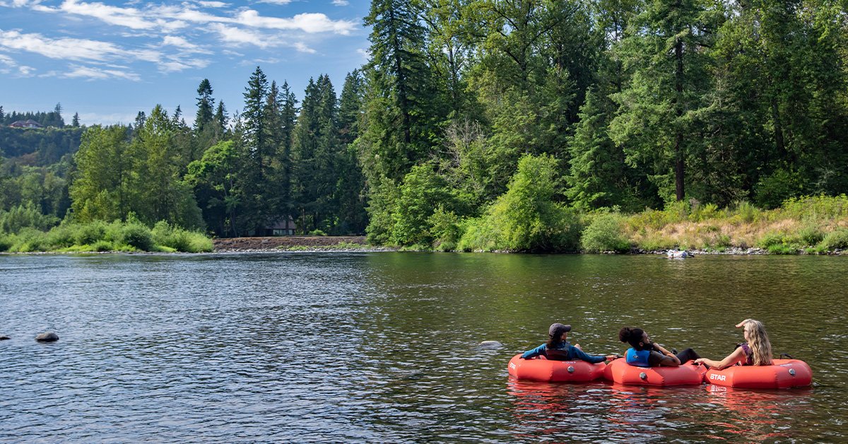 A trio of people in red inner tubes floating down a river on a beautiful summer day in the Mt Hood Territory
